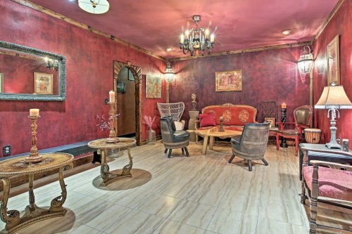 Cozy living room with red walls, vintage furniture, a chandelier, and decorative art pieces. Warm and inviting atmosphere.