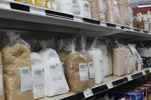 Shelves stocked with various types of packaged sugar, including white, brown, and powdered varieties.