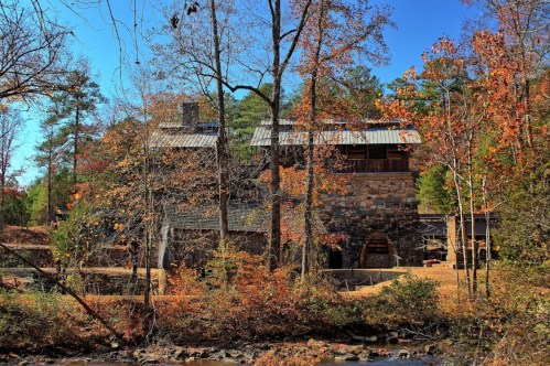 A rustic stone building surrounded by autumn trees and a clear blue sky, next to a flowing stream.
