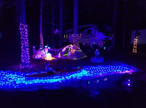 A nighttime scene with colorful lights, a kayak on a glowing blue river, and festive decorations among trees.