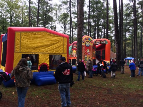 A colorful bounce house and inflatable slide in a wooded area, with people enjoying a festive outdoor event.