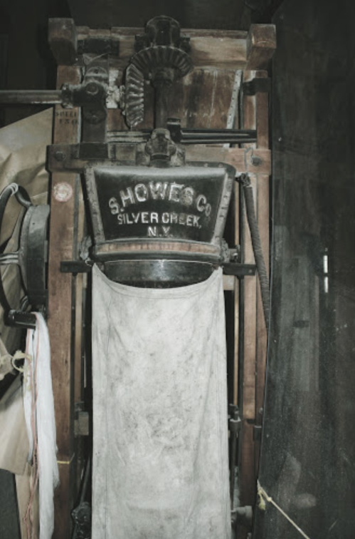 An old printing press with the inscription "S. Howes Co. Silver Creek, N.Y." displayed in a dimly lit setting.