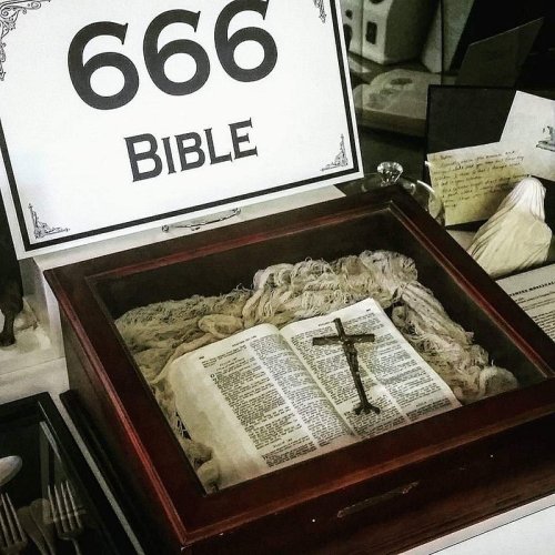 A display featuring a Bible labeled "666" inside a wooden box, with a cross and fabric surrounding it.