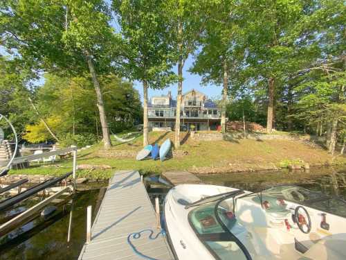 A serene lakeside view featuring a house, dock, and kayaks surrounded by lush greenery.