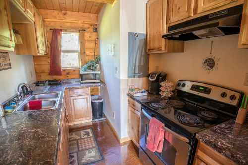 Cozy kitchen with wooden cabinets, a stove, sink, and coffee maker, featuring a warm, rustic design.