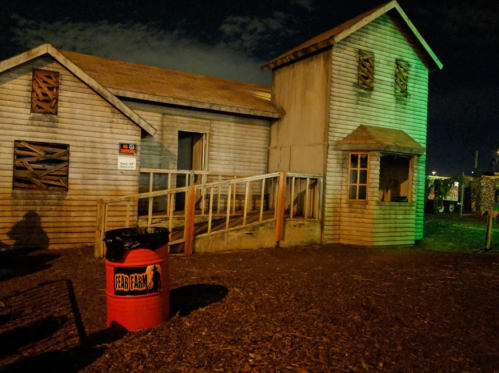 A spooky, dimly lit farmhouse with boarded windows and a red trash can labeled "Fear Farm" in the foreground.