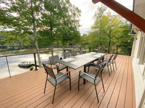 A spacious deck with a large table and chairs overlooking a calm lake surrounded by trees.