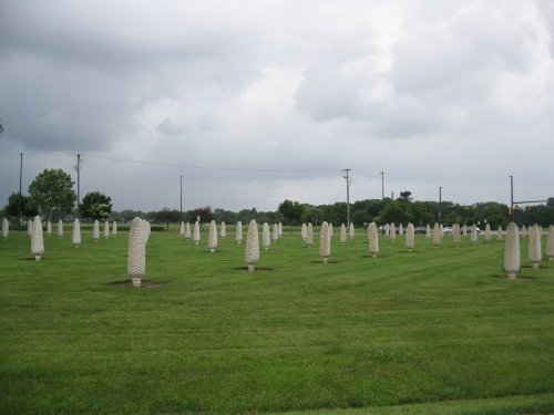 A grassy field with numerous white stone sculptures arranged in rows under a cloudy sky.