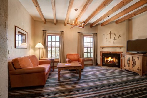 Cozy living room with leather furniture, a fireplace, and wooden beams, featuring a striped rug and large windows.