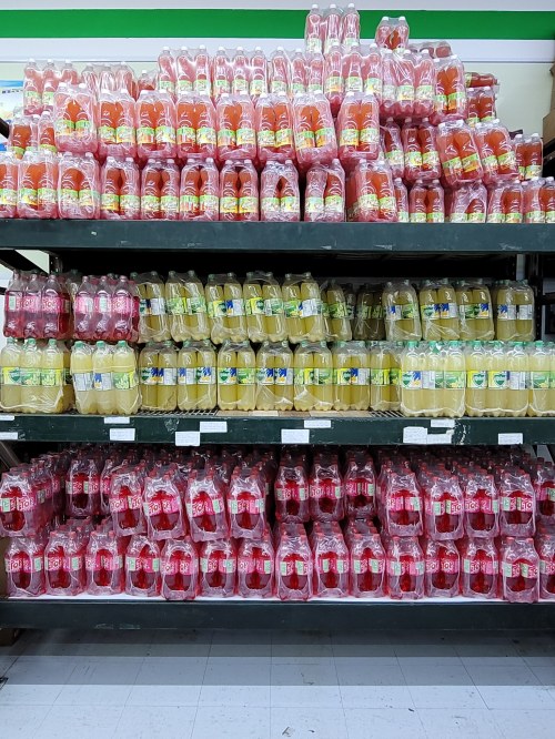 Shelves stacked with colorful bottles of various soft drinks, including red and yellow varieties.