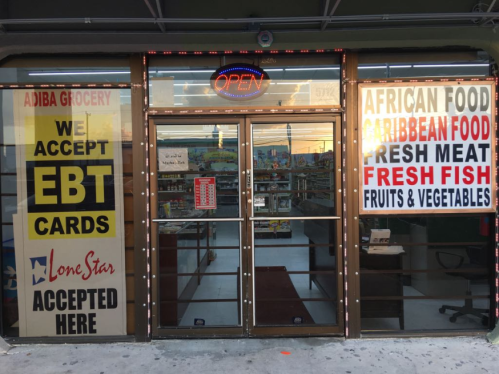 Storefront with glass doors displaying signs for EBT acceptance, African and Caribbean food, fresh fish, and groceries.