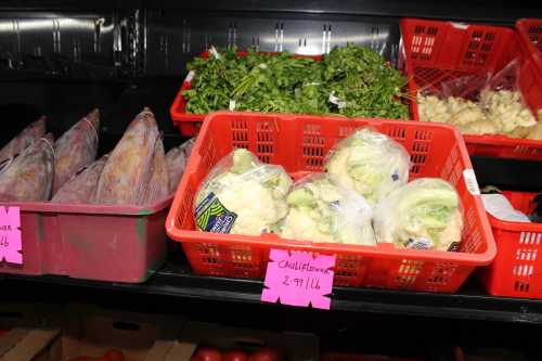 Baskets of fresh vegetables, including cauliflower and herbs, displayed in a grocery store. Price tags visible.