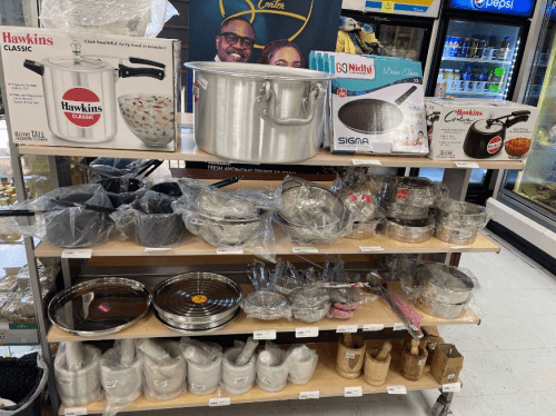 A display of various cooking pots and pans on a shelf in a store, with packaging and labels visible.