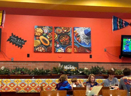 Colorful restaurant interior featuring vibrant food art on the wall and patrons dining at tables below.