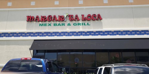 Sign for "Margarita Loca Mex Bar & Grill" on a building, with parked cars in front.
