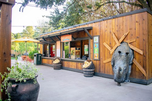 A wooden food stand with a boar sculpture on the wall, surrounded by greenery and outdoor seating.