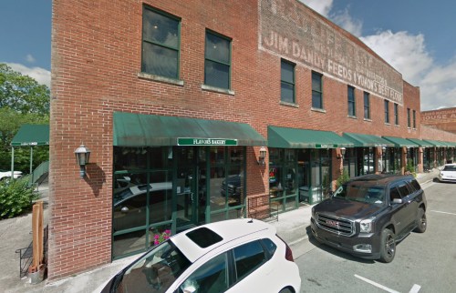 Brick building with green awnings, featuring a bakery and parked cars in front under a blue sky.