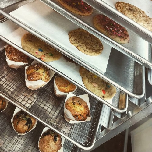 A tray of freshly baked cookies and muffins on a cooling rack, some with colorful toppings and wrappers.