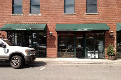 A brick building with two storefronts: "Flavors Bakery" and "Flavor Ice Cream," with green awnings and a parked white truck.