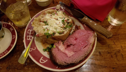 A plate with a baked potato topped with sour cream and chives, alongside a serving of pink roast beef.