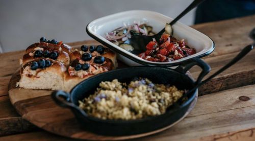 A wooden platter with blueberry-topped bread, a fresh salad, and a dish of savory grains.