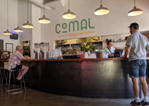A modern food incubator with a curved counter, patrons seated, and staff preparing food in a bright, inviting space.