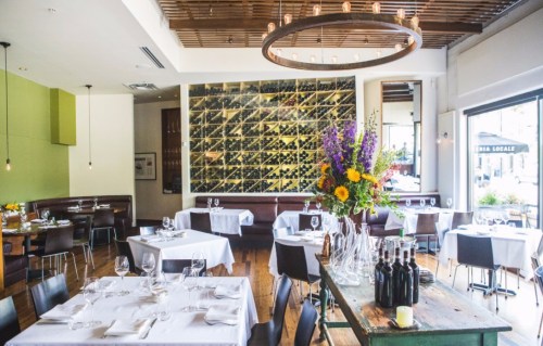 A modern restaurant interior with tables set for dining, a wine wall, and a colorful flower arrangement.