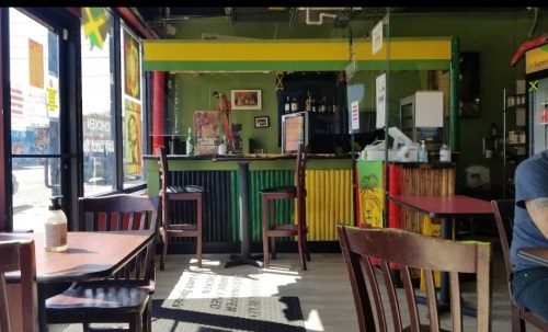 A colorful restaurant interior with a bar, wooden tables, and chairs, featuring green and yellow decor.