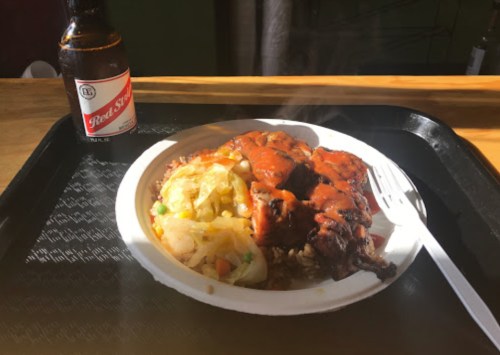 A steaming plate of food with chicken and sauce, alongside a bottle of Real Steel beer on a tray.