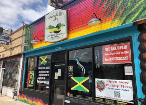 Colorful exterior of Jamaican Grille with a sign indicating it's open and offers delivery through DoorDash.