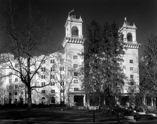 Historic building with two towers, surrounded by trees, captured in black and white.