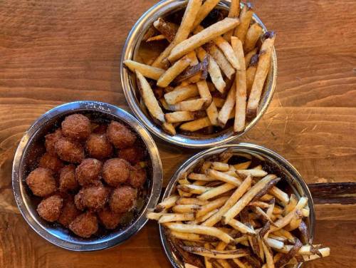 Three bowls on a wooden surface: one with crispy fries, one with thin fries, and one with golden-brown fried balls.