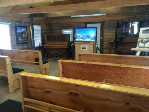 Interior of a rustic room with wooden benches, a TV, and displays, resembling a small museum or gathering space.
