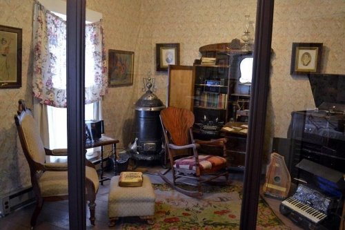 A vintage room with a rocking chair, bookshelves, and various musical instruments, surrounded by floral wallpaper.