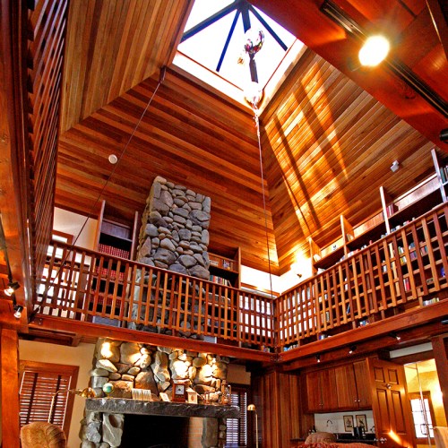 A spacious wooden interior of a library with a stone fireplace and a high ceiling featuring a chandelier.