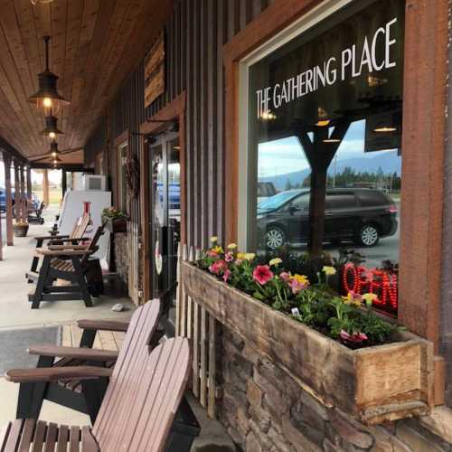 A rustic storefront with wooden chairs and flower boxes, featuring a sign that reads "The Gathering Place" and an open sign.