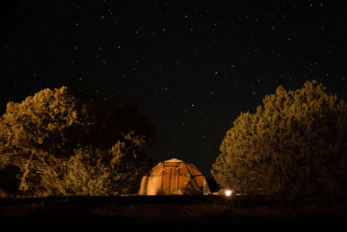 A wooden yurt surrounded by trees under a starry night sky.