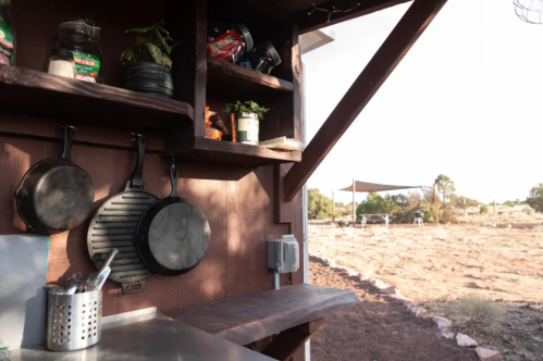 A rustic outdoor kitchen with hanging pots and a view of a desert landscape in the background.