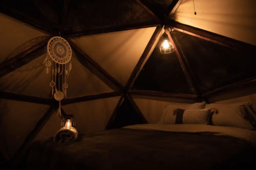 Cozy interior of a geodesic dome with a bed, dreamcatcher, and warm lighting.