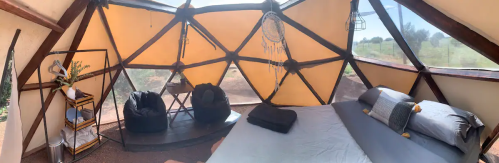 Cozy interior of a geodesic dome with a bed, bean bags, and natural light streaming through the windows.