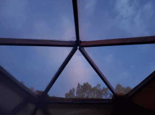 View of a geometric glass roof against a twilight sky with scattered clouds and tree silhouettes in the background.