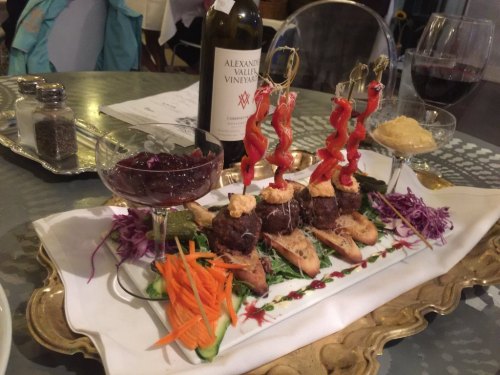 A beautifully arranged platter with meatballs, garnishes, and sauces, accompanied by wine and elegant glassware.