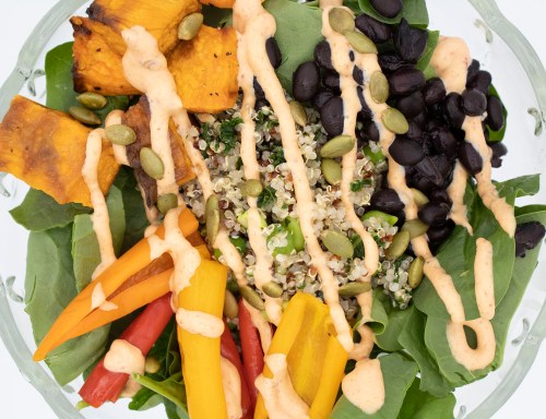 A colorful salad with spinach, quinoa, black beans, roasted squash, and drizzled with a creamy dressing.