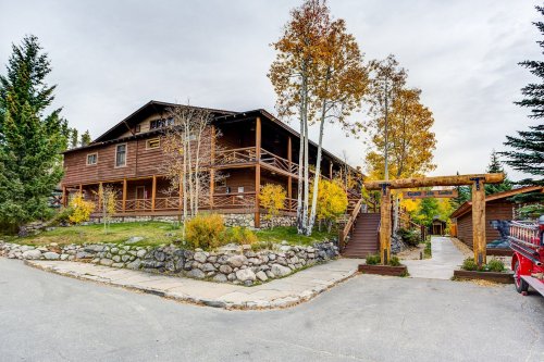 A rustic wooden lodge surrounded by autumn trees, with a stone pathway and welcoming entrance.