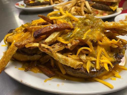A plate of a burger topped with melted cheese, crispy fries, and green chili sauce.