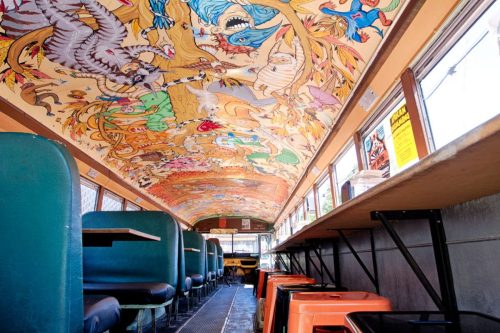 Interior of a colorful bus with a vibrant, illustrated ceiling and seating along the sides.