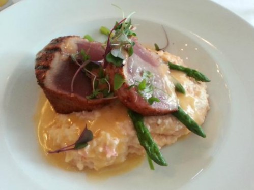 A plate featuring seared tuna on a creamy base, topped with asparagus and microgreens, drizzled with sauce.