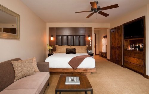 A cozy hotel room featuring a king bed, sofa, wooden furniture, and a flat-screen TV. Warm, inviting decor.