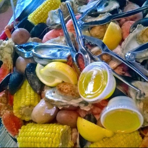 A seafood platter featuring shrimp, crab, mussels, corn, and lemon wedges, with dipping sauces and seafood tools.
