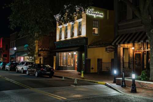 A quiet street at night featuring a restaurant, parked cars, and streetlights illuminating the scene.